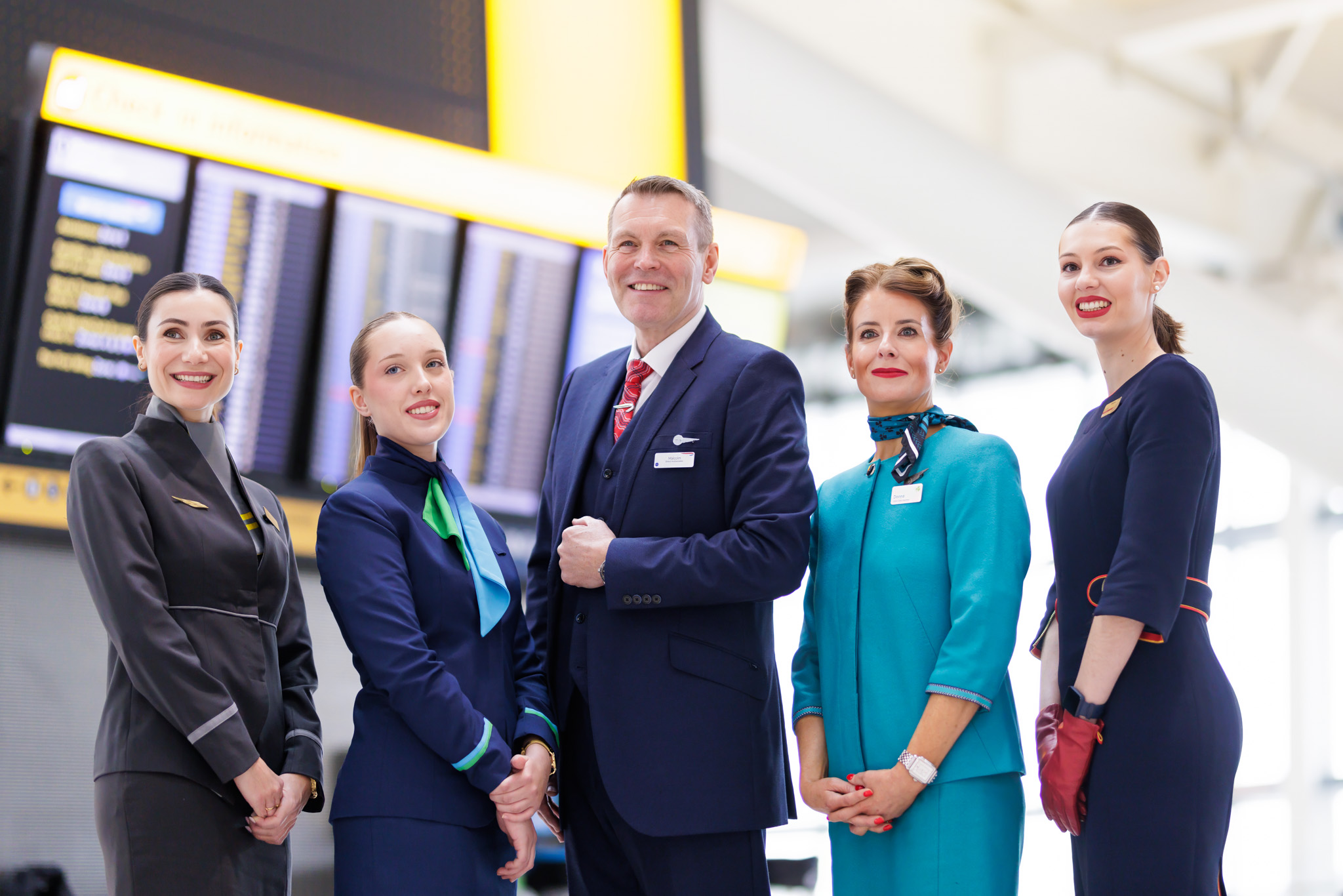 Members of cabin crew of IAG airlines posing by screens at Heathrow